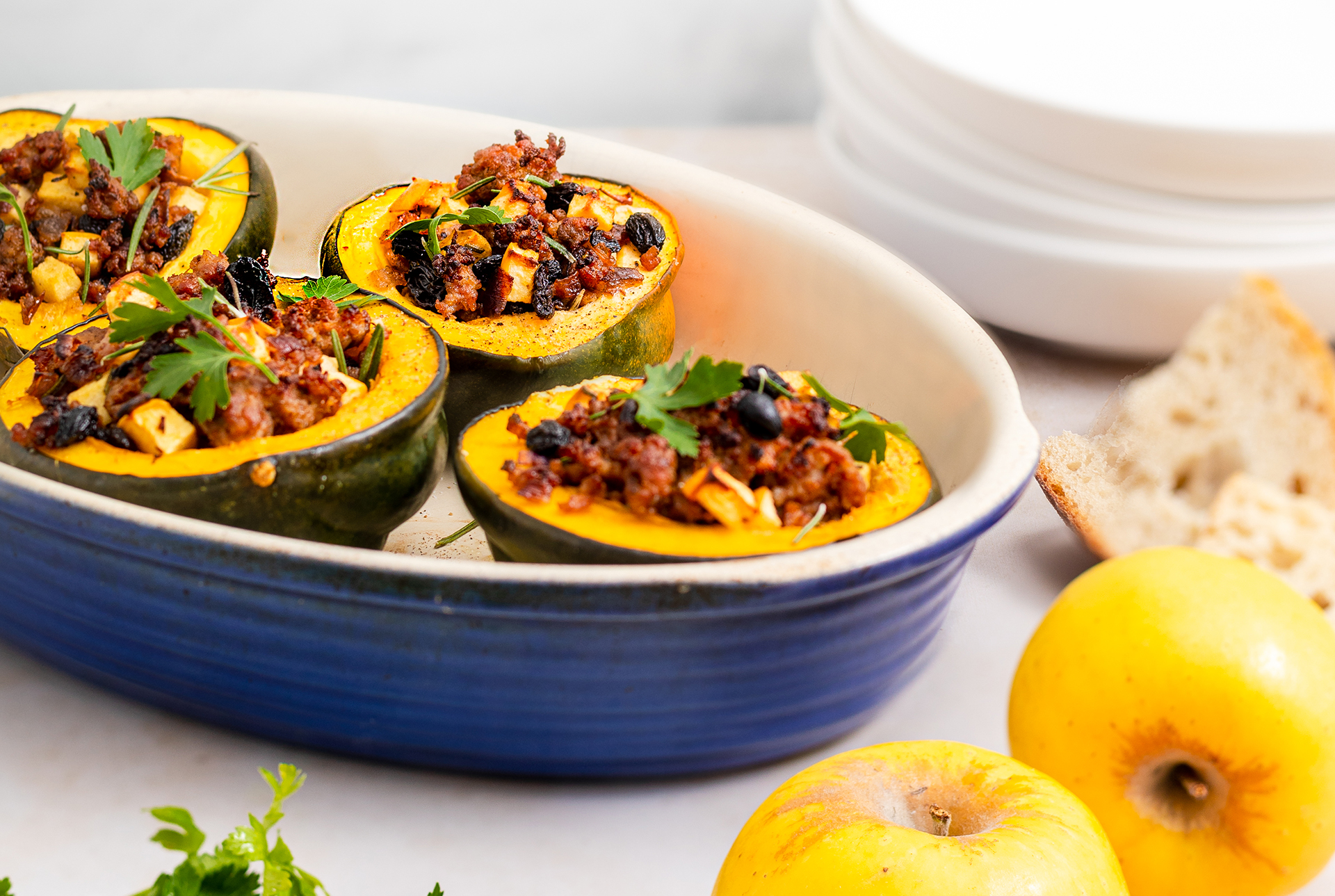 Four acorn squash carved out with a meat and apple filling next to Opal Apples on the plate. 